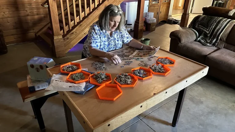 A woman piecing together a large complicated puzzle on a puzzle-games table